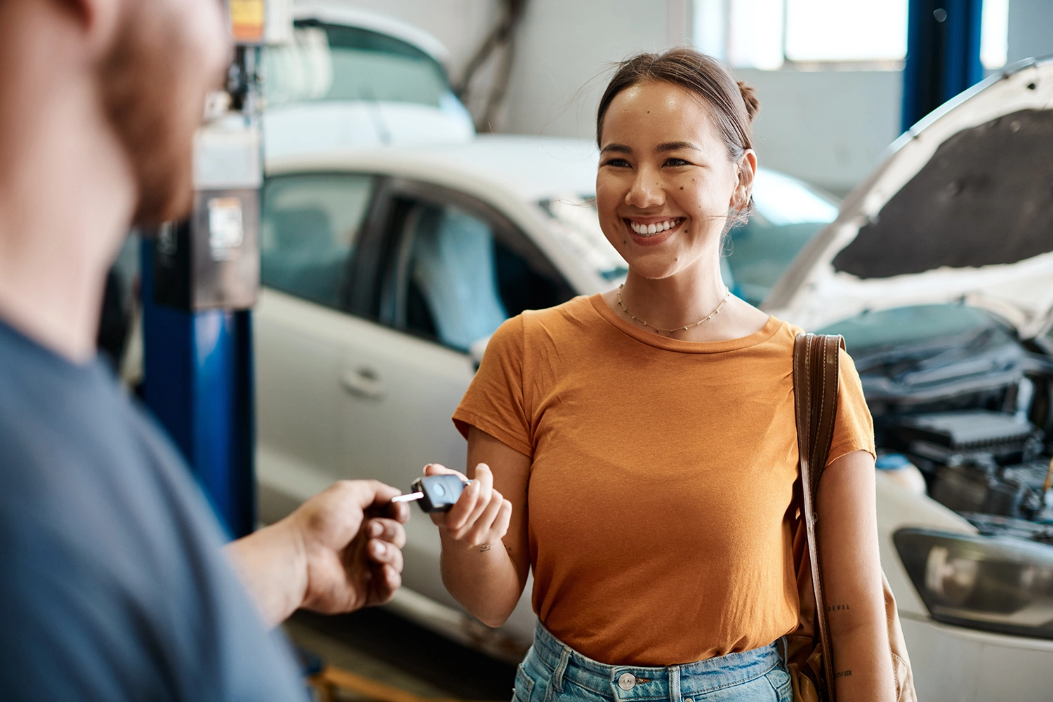 An autobody repair specialist hands a smiling woman her car key.